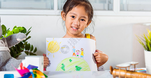 小女孩举起多彩多彩的绘画家庭 站在地球上手牵手 在纸上拍摄图片