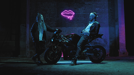 一个骑超运动摩托车的家伙 站在一个女孩对着粉红亮号说话街道速度骑士行动恋人车轮女士城市摩托桦木图片