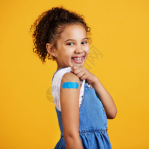 工作室肖像混血女孩在她的手臂上显示了一块石膏 与黄色背景隔离 可爱的西班牙裔儿童举起袖子展示 covid 或 corona 刺戳图片