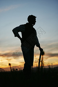 一个男性农民用耙子站在田里的轮廓 一个男人准备在清晨去农场工作图片
