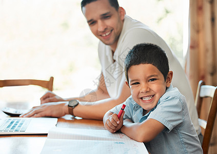 当爸爸远程工作时 兴奋的学龄前男孩在家里的桌子上用蜡笔画画和写字 在线教育课程中与父母坐在一起的孩子图片