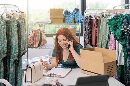 年轻的女商务人士微笑着 在她的服装店的仓库里用智能手机与她的供应商和顾客交谈 工作和经营理念图片
