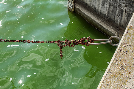 旧的生锈船链 在码头绿水上 海平面指标为背景图片