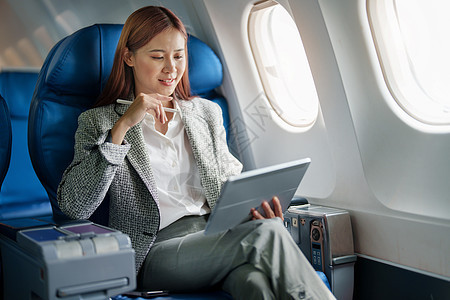 一位成功的亚洲女商务人士或女企业家在飞机上穿着正式西装的肖像坐在商务舱的座位上 并在飞行期间使用平板电脑电话女士课程商务旅行套装图片