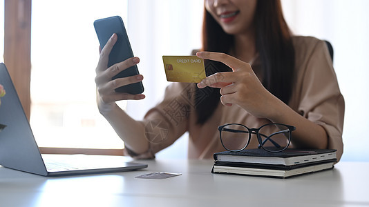 快乐的亚洲女性持有者信用卡 并在线付款或网上银行 在智能手机上图片