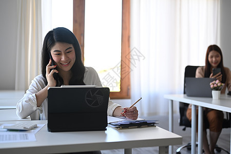 勤奋的亚洲女性办公室工作人员在移动电话上交谈 并使用计算机平板电脑图片