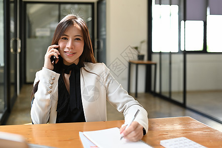 坐在现代工作场所和谈手机的成功女商务人士图片