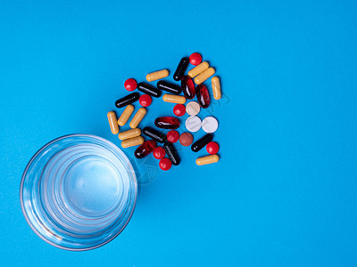 顶端有一杯水 旁边是多色药丸和胶囊剂量药片治疗玻璃药剂制药疾病帮助化学药物图片