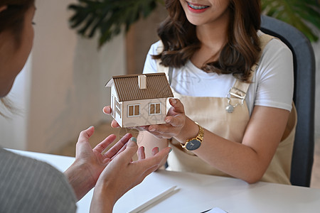 裁剪拍摄的房地产经纪人持有房屋模型并向客户提出建议图片