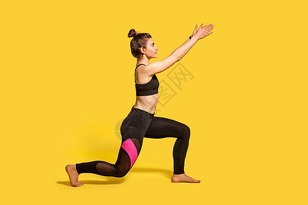 年轻女性在黄色背景的室内运动体操瑜伽发髻瑜珈裤弓步肌肉训练女士损失身体图片