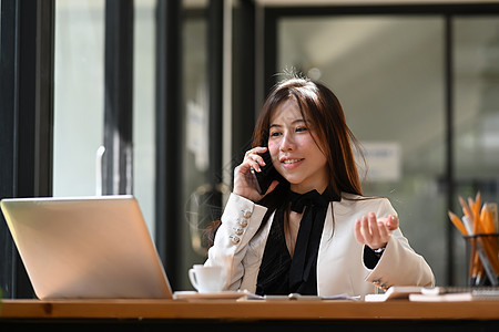 有吸引力的女商务人士在智能手机上交谈 并用笔记本电脑工作图片