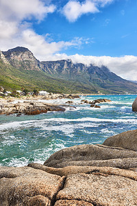 南非开普敦坎普斯湾的海洋海滩 大海 云彩 蓝天与复制空间的景观 潮汐冲刷着海岸线的岩石或巨石 十二门徒山背景图片