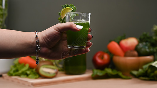 女士手握着新鲜绿色脱毒蔬菜汁的杯子 健康饮品概念图片