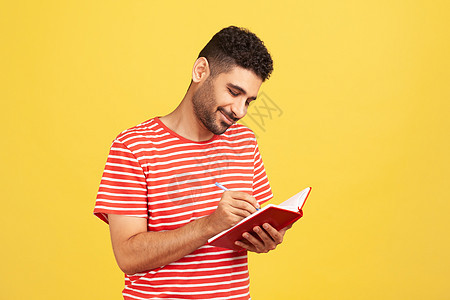 穿着红色T恤穿黄色背景的情绪年轻男子男人商业待办记事本作家笔记铅笔广告日程规划师图片