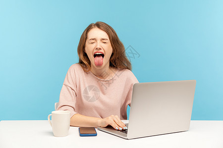 情感年轻女性在蓝背景的笔记本电脑上工作傻子举止人士蓝色厌恶博主商务嘲笑女孩办公室图片