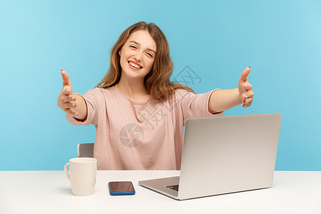 情感年轻女性在蓝背景的笔记本电脑上工作接待员微笑脾气拉伸好客秘书商业接待人士手臂图片