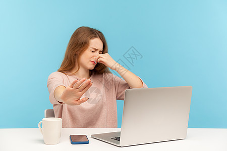 情感年轻女性在蓝背景的笔记本电脑上工作厌恶斥力蓝色商务呼吸鼻子办公室自由职业者女士商业图片