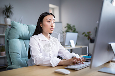 穿着现代服装在电脑前工作的韩国女商务人士 穿着白衬衫在键盘上打字的亚洲女性图片