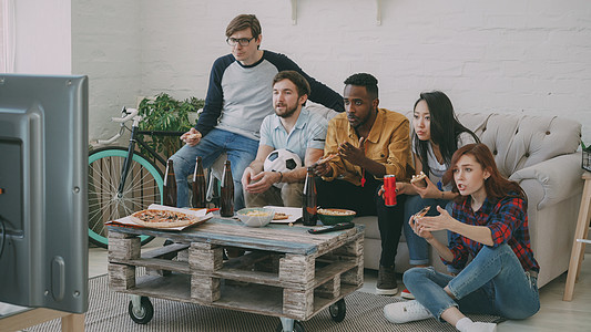 多种族朋友运动球迷团体在电视上观看足球锦标赛 一起吃比萨 在家喝啤酒; 在图片