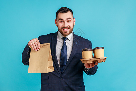 快乐的笑脸长胡子的男人穿着正式的风格西装 拿着纸包 把咖啡拿在手上 快递 早餐图片