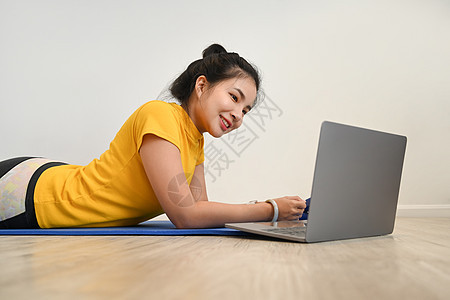 在公寓健身期间在笔记本电脑上观看在线辅导课程的体育女年青女子图片