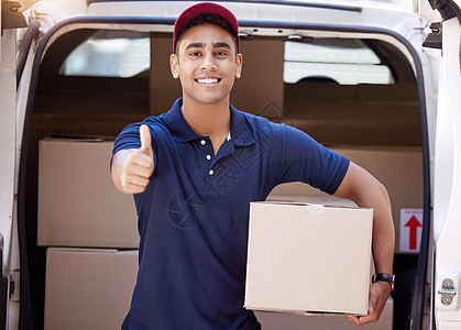 一位年轻送货员的肖像 在装箱时举起拇指来 从货车上卸下箱子图片