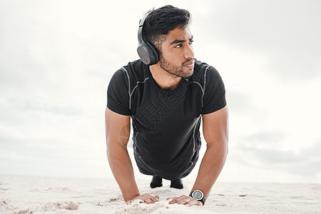 你的锻炼会很有趣 只是加上音乐 一个运动的年轻人穿着耳机在沙滩上做推车图片