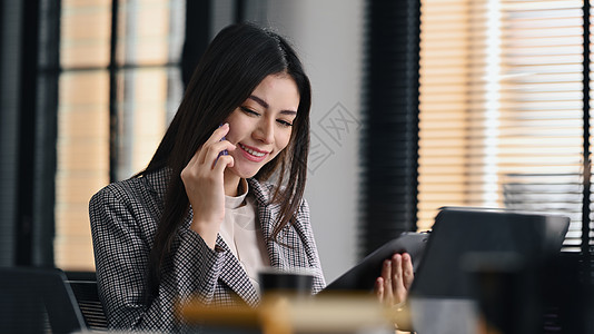 年轻的女性财务顾问与客户通过手机交谈 并在办公室使用笔记本电脑图片