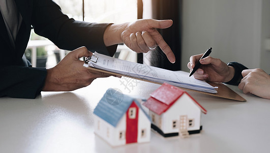 房地产经纪人与房屋模型手签合同 有合同保护它 在办公室签署适度的协议表 概念房地产 搬家或租房房子代理人交易审核销售贷款签名文档图片