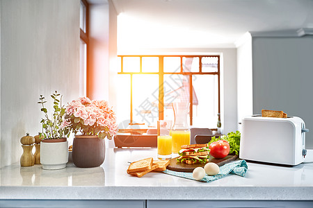 白色电动面包面包机 橙汁和三明治放在厨房桌上 早餐在舒适的厨房里 太阳耀斑咖啡盘子玻璃厨具木头甜点机器水果桌子果汁图片