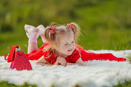 穿红裙子的女孩躺在白毯子上公园后院微笑孩子们女性闲暇乐趣工具草地享受图片