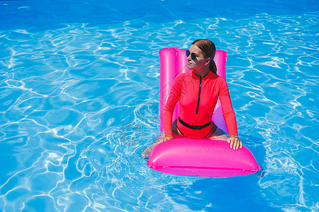 身着太阳镜和粉红色比基尼的快乐年轻女子 漂浮在游泳池边可充气床垫上派对海滩游泳衣游泳棕褐色泳装天线假期身体女士图片