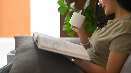 喝热茶和在家舒适沙发上读书的亚洲平静女性;图片