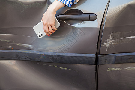 手机和被损坏的汽车 女性持有手机碰撞危险驾驶车身事故划痕运输挡泥板保险城市图片