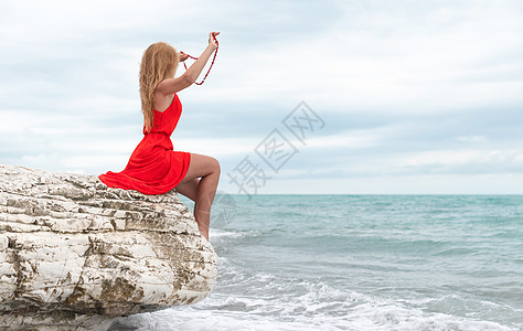 夏天在海边的白色岩石上 穿着红裙子的美女太阳海滨外貌闲暇自由日光浴快乐海岸蓝色女孩图片