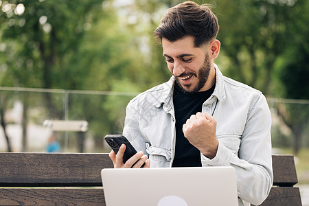 在手机上享受成功的快乐亚美尼亚商务人士的画像 特写快乐大胡子的家伙在智能手机上阅读好消息 大胡子男子在智能手机上庆祝胜利 大吃一图片