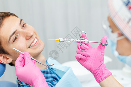 身穿粉红色手套的医生拿着注射器 带着麻醉剂和镜像与年轻人在背景上微笑图片