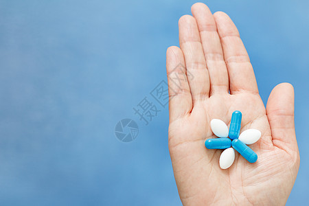 握着蓝色和白色药片的手贴近镜头图片