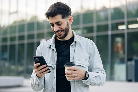 在智能手机短信上使用社交媒体应用软件的年轻优雅胡子男子在户外获得微笑的新闻 人民肖像画 技术男人电话时尚街道混血风格城市互联网校图片