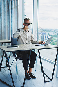 戴眼镜的自由职业者在笔记本电脑上工作并喝咖啡 经理坐在办公室的桌子旁 在笔记本电脑上工作 自由职业者工作场所 远程工作的员工技术图片