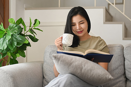 年轻女孩喝热茶 在家里沙发上读有趣的书图片