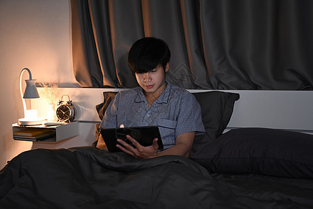 穿着睡衣的年轻人在床上用数字平板电脑图片