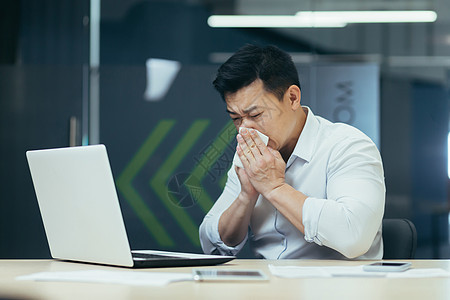 办公室的病人咳嗽和流鼻血 亚洲商务人士在办公室用笔记本电脑做冷工痛苦经理人士组织商业餐巾男性工作手帕桌子图片
