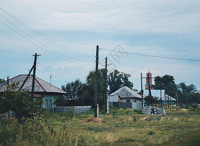 俄罗斯一个村庄蓝天多云的东正教教堂背景下的老房子和电线杆图片