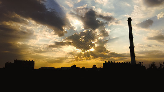锅炉房的烟囱和建筑物的轮廓在美丽的云彩和背后的太阳的衬托下 阳光穿透云层工厂阴影天际环境蓝色地平线天空工业黄色技术图片