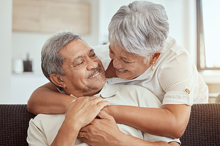 混血老年夫妇在家里的客厅里拥抱 微笑的老年丈夫和妻子在休息室互相拥抱拥抱 快乐嬉戏的退休男女结合并感受到爱图片
