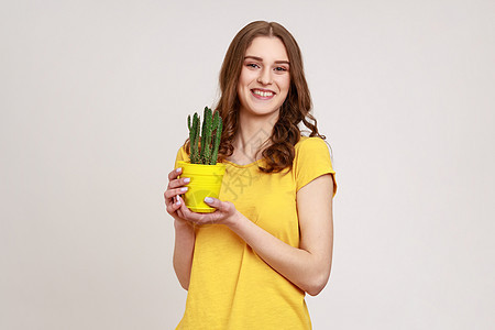 穿着黄色T恤的年轻女子肖像 带着仙人掌拿着花盆 看着有牙笑的照相机 (笑声)图片
