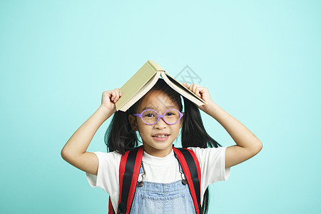孩子们去上学 女孩滑稽地笑着 孩子们戴着眼镜的女孩把书放在头上老师童年小学生班级孩子社会女儿家庭作业学校概念图片
