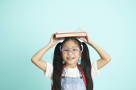 孩子们去上学 女孩滑稽地笑着 孩子们戴着眼镜的女孩把书放在头上微笑瞳孔学校概念家庭作业电脑班级社会学生老师图片