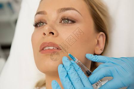 美丽的年轻女子在脸上注射美容针时药物塑料美容师液体医生手套护理沙龙治疗病人图片